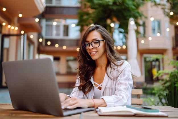 Mujer sonriente sentada en el café y trabajando en la computadora portátil Concepto de educación en línea independiente