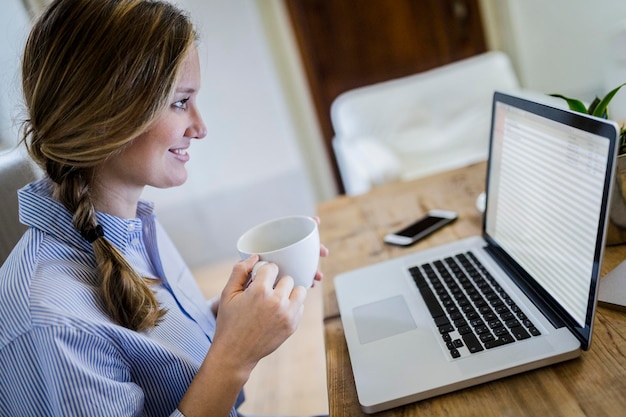 Mujer sonriente sentada en el escritorio con una taza de café y una computadora portátil