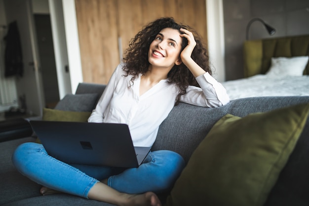 Mujer sonriente sentada con un portátil en el sofá