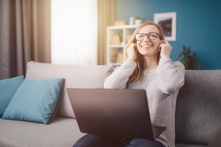 Mujer sonriente sentada en el sofá con auriculares y usando una computadora portátil