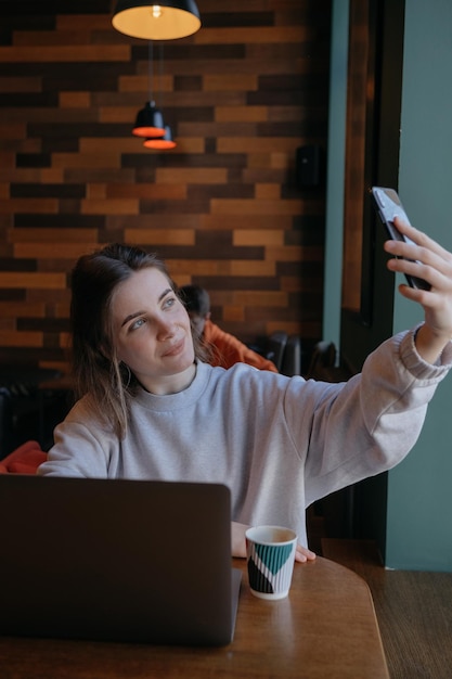 Mujer sonriente sentada en el sofá de la cocina hablando por videollamadas en línea mirando el teléfono