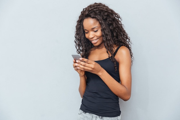 Mujer sonriente con smartphone sobre pared gris