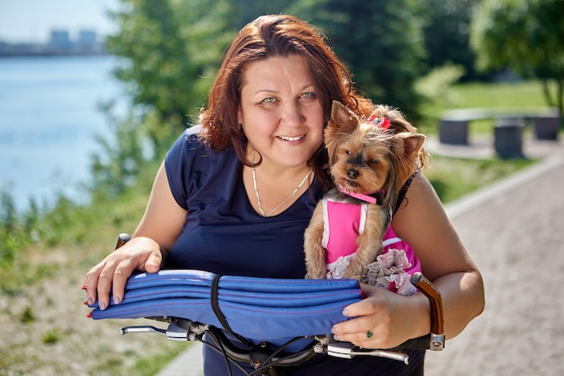 Mujer sonriente con sobrepeso con yorkshire terrier en manos en el jardín