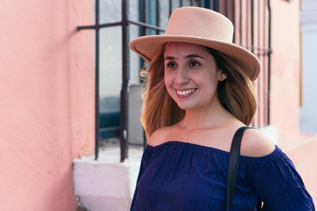 Mujer sonriente con sombrero en la cabeza mientras está de pie en la calle