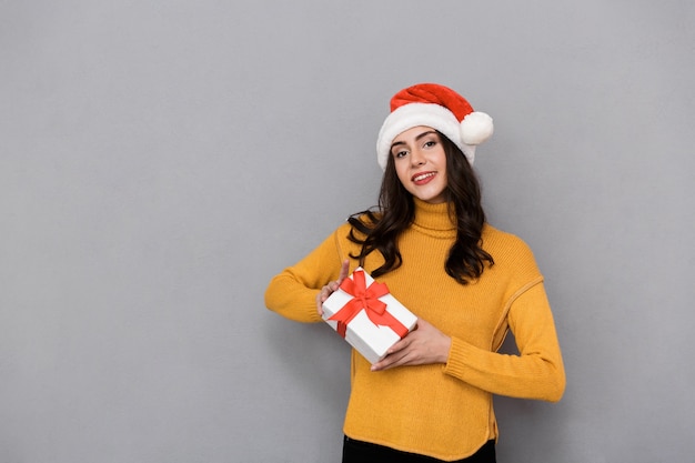 Mujer sonriente con sombrero de navidad que se encuentran aisladas sobre fondo gris, sosteniendo el cuadro actual