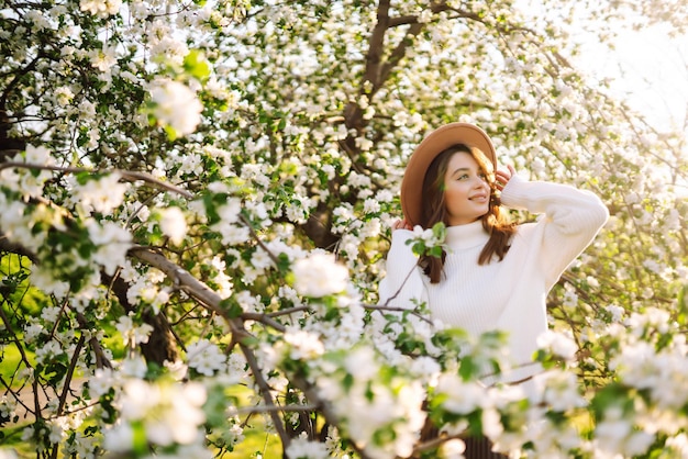 Mujer sonriente con sombrero posando en el floreciente parque de primavera El concepto de viajes relajantes Estilo de moda