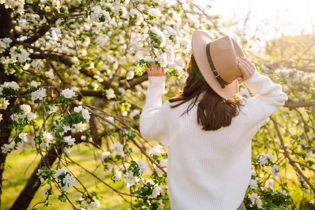 Mujer sonriente con sombrero posando en el parque de primavera en flor El concepto de viaje relajante Estilo de moda