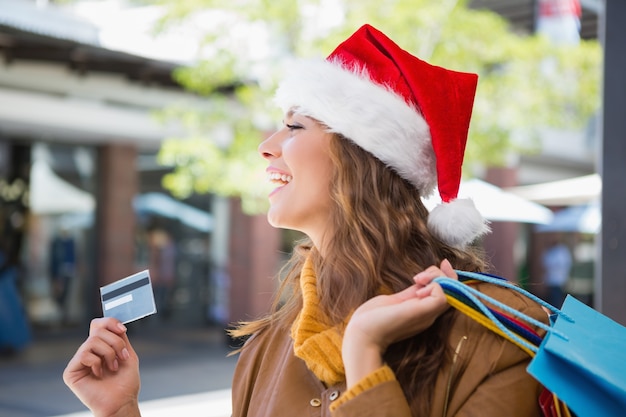 Mujer sonriente con sombrero de santa y bolsas de compras