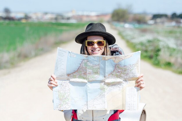 Mujer sonriente con sombrero sosteniendo un mapa en una carretera