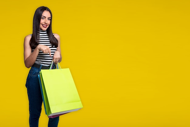 Mujer sonriente sosteniendo bolsas de la compra, aislado sobre fondo amarillo con espacio para texto.