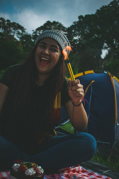 Foto mujer sonriente sosteniendo una chispa encendida contra los árboles