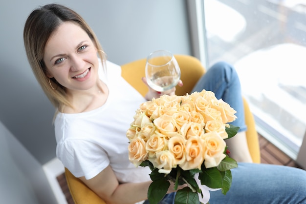 Mujer sonriente sosteniendo una copa de vino y un ramo de flores en sus manos