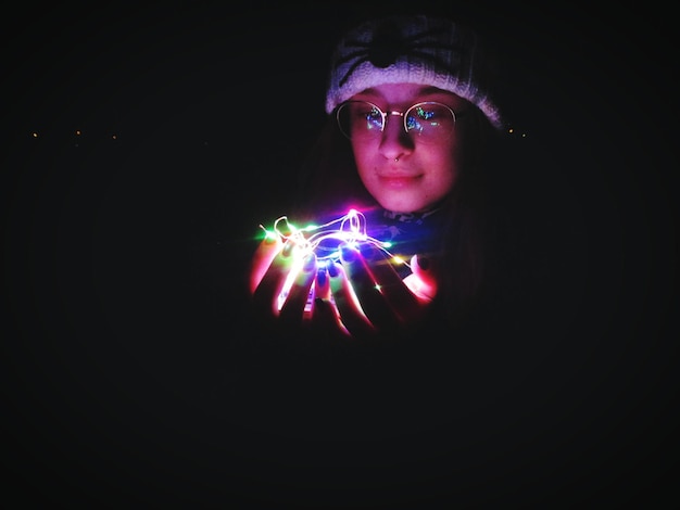 Foto mujer sonriente sosteniendo luces de hadas en la oscuridad