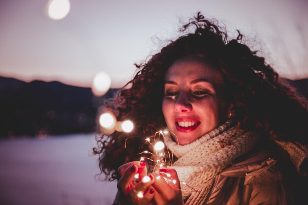 Foto mujer sonriente sosteniendo luces iluminadas contra el cielo
