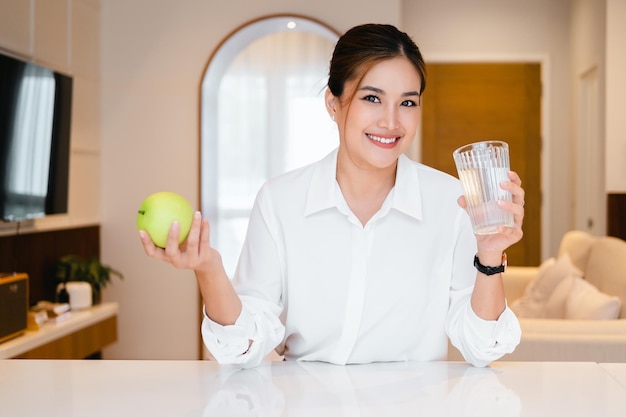 Mujer sonriente sosteniendo en las manos un vaso de agua y una manzana verde fresca Concepto de dieta