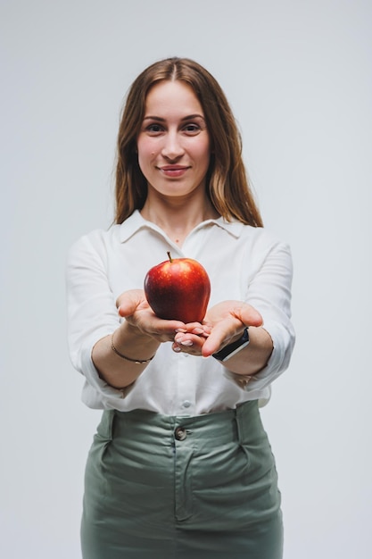 Mujer sonriente sosteniendo una manzana roja Hermosa morena con una camisa blanca Alimentos saludables para plantas y vitaminas Fondo blanco