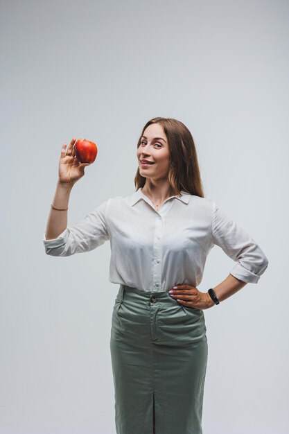 Mujer sonriente sosteniendo una manzana roja Hermosa morena con una camisa blanca Alimentos saludables para plantas y vitaminas Fondo blanco