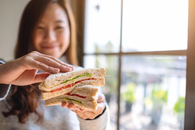 Foto mujer sonriente sosteniendo un sándwich junto a la ventana