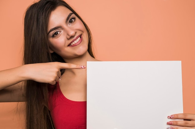 Mujer sonriente sosteniendo y señalando con el dedo en una cartelera blanca para un cartel publicitario.