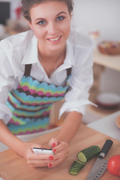 Mujer sonriente sosteniendo su celular en la cocina