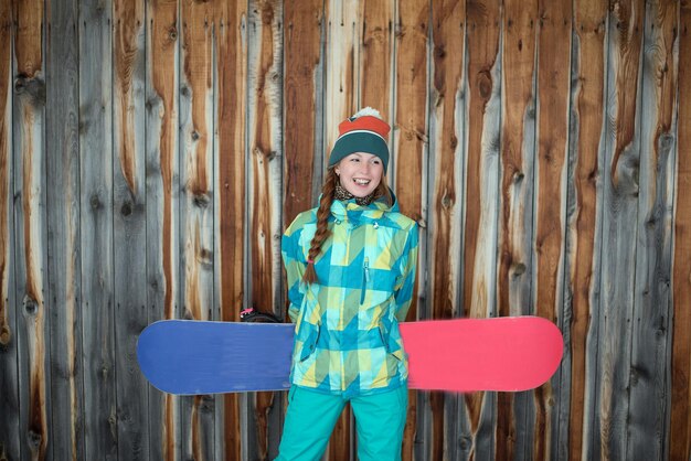 Foto mujer sonriente sosteniendo una tabla de nieve mientras está de pie en una cabaña de madera