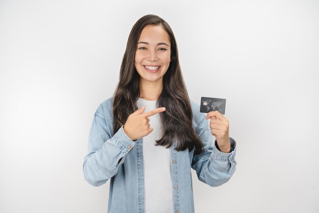 Mujer sonriente sosteniendo una tarjeta de crédito dorada y señalando con el dedo aislado de fondo blanco