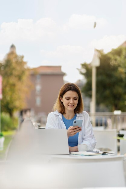 Mujer sonriente sosteniendo un teléfono inteligente usando la comunicación de aplicaciones móviles en línea en la calle