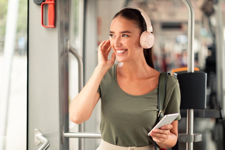 Mujer sonriente sosteniendo teléfono móvil y usando auriculares en tranvía