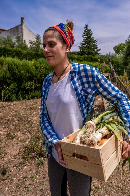 Foto mujer sonriente sosteniendo verduras de pie en la granja