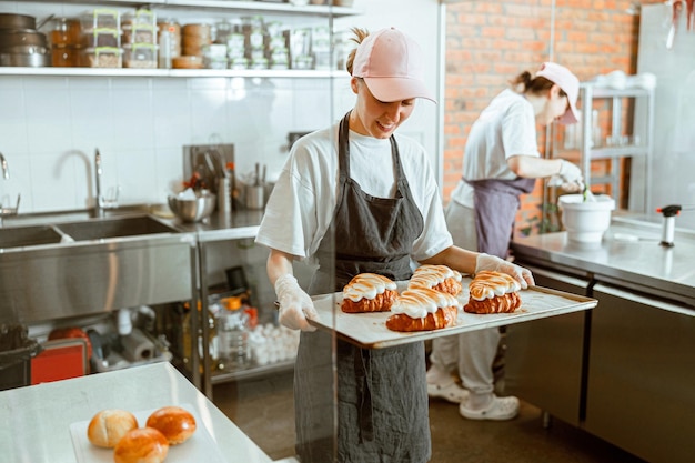 Mujer sonriente sostiene la bandeja con deliciosos croissants decorados con crema quemada en panadería artesanal