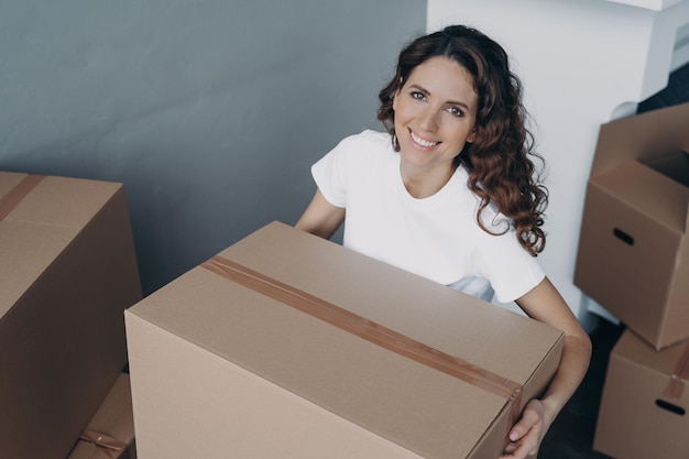 Mujer sonriente sostiene un paquete de caja de cartón Reubicación fácil Publicidad de servicio de mudanza o entrega