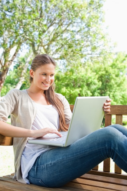 Mujer sonriente con su computadora portátil que se sienta en un banco