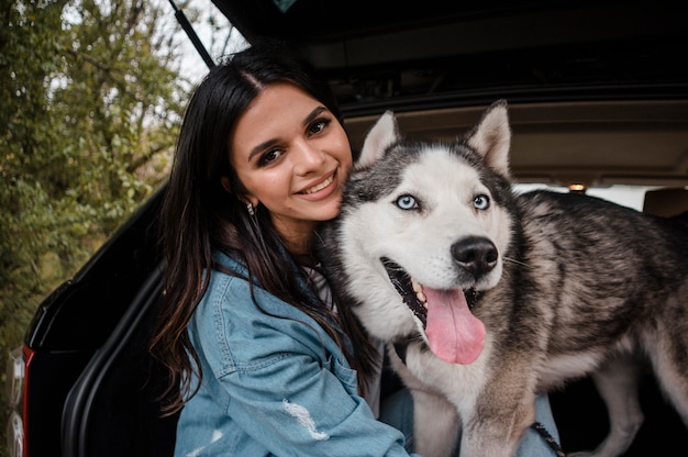 Mujer sonriente con su lindo husky viajando en coche