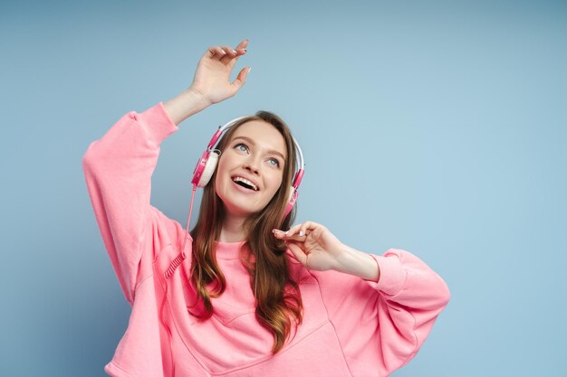 mujer sonriente en sudadera rosa bailando escuchando música en auriculares aislados