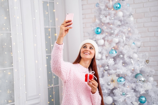 Mujer sonriente con un suéter y un sombrero tomando un selfie