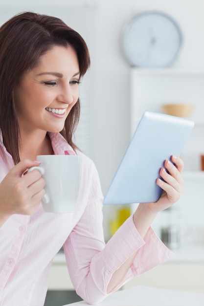 Mujer sonriente con taza de café mirando tableta digital