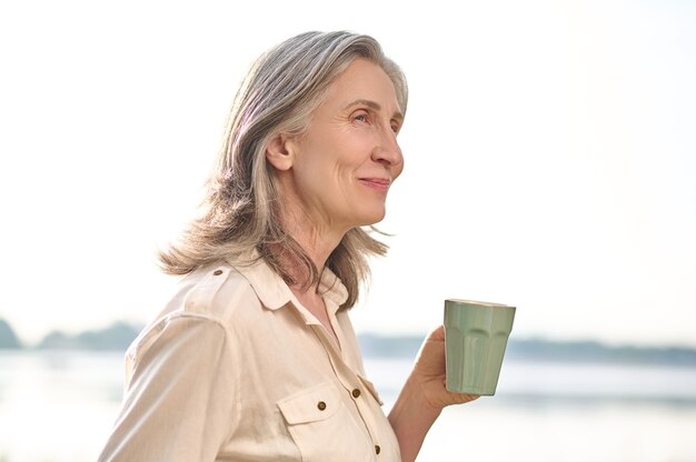 Mujer sonriente con una taza de café en la naturaleza