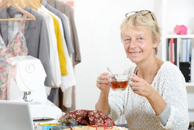 Una mujer sonriente con una taza de té en su taller de costura