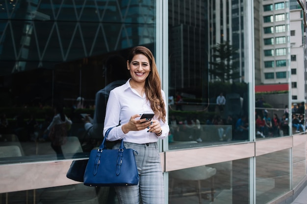 mujer sonriente, con, teléfono, exterior, edificio de oficinas