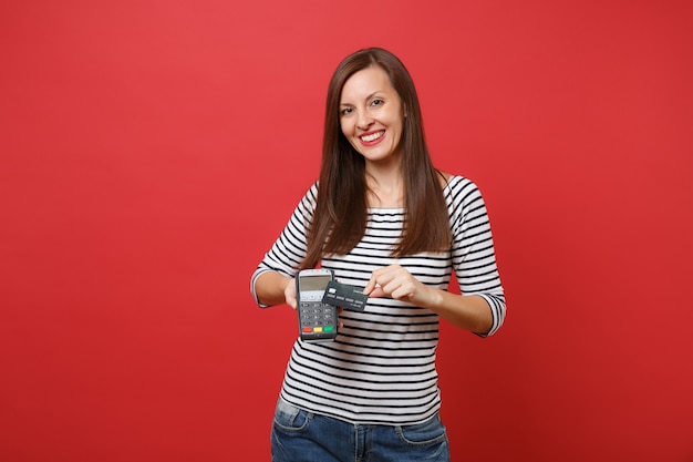 Mujer sonriente con terminal de pago bancario moderno inalámbrico para procesar y adquirir pagos con tarjeta de crédito, tarjeta negra aislada sobre fondo rojo. Personas sinceras emociones, estilo de vida. Simulacros de espacio de copia.