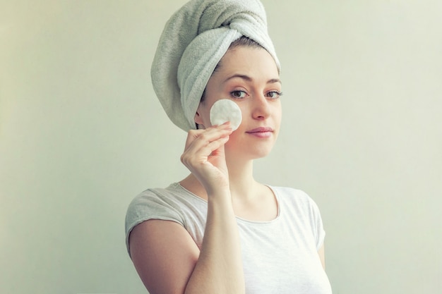 Mujer sonriente en una toalla en la cabeza con una piel suave y sana eliminación de maquillaje con algodón aislado