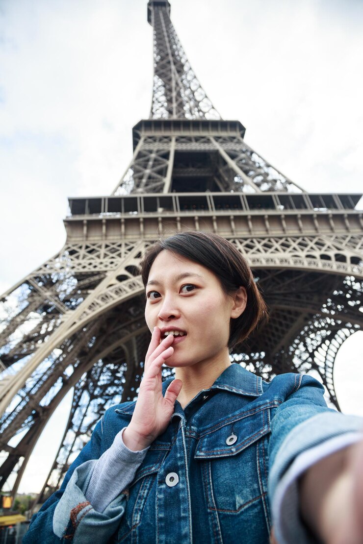 Foto mujer sonriente tomando una selfie contra la torre eiffel