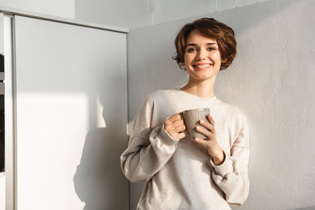 Mujer sonriente tomando una taza de té en la cocina por la mañana