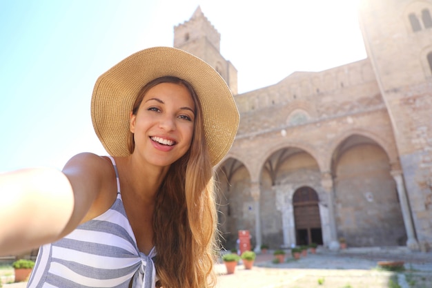 Mujer sonriente tomar selfie con la Catedral de Cefalu en Sicilia, Italia