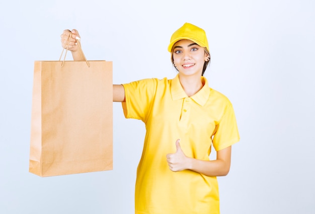 Una mujer sonriente en uniforme amarillo con una bolsa de papel artesanal en blanco marrón mostrando un pulgar hacia arriba.