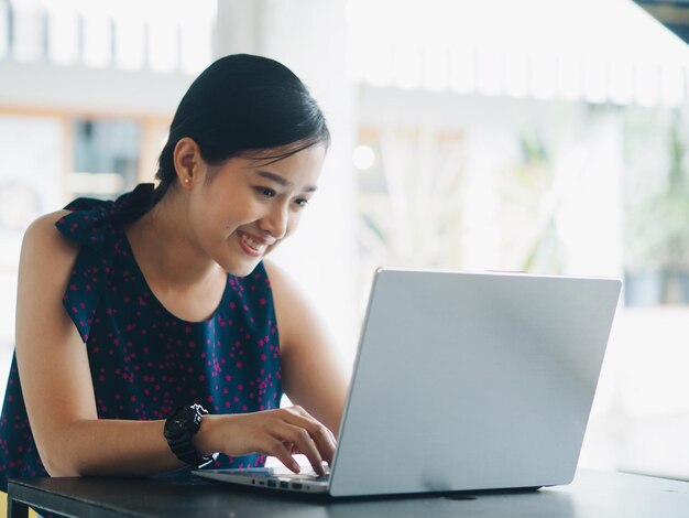 Mujer sonriente usando una computadora portátil mientras está sentada en la mesa