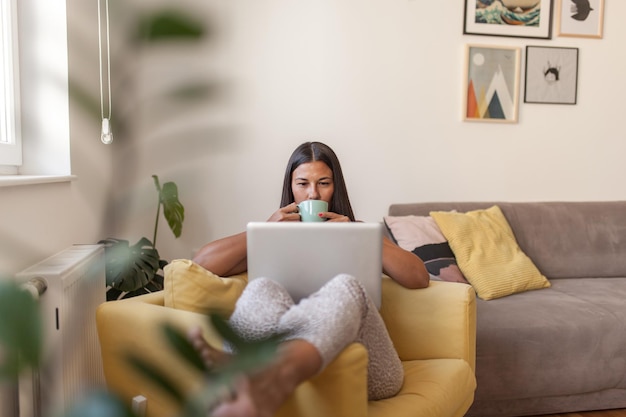 Mujer sonriente usando una computadora portátil mientras está sentada en el sofá en casa