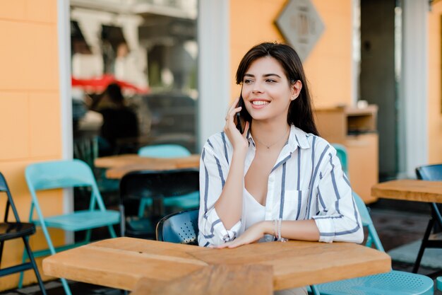 Mujer sonriente utiliza teléfono sentado en la cafetería