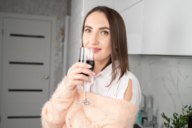 Mujer sonriente con vaso de vino tinto de pie en la cocina.