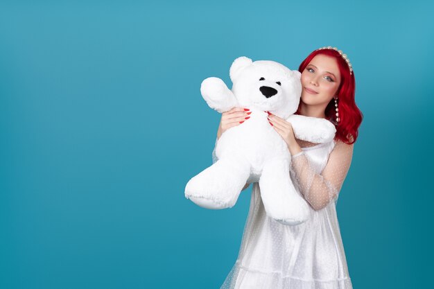 Mujer sonriente con un vestido blanco presiona un gran oso de peluche blanco en su cara